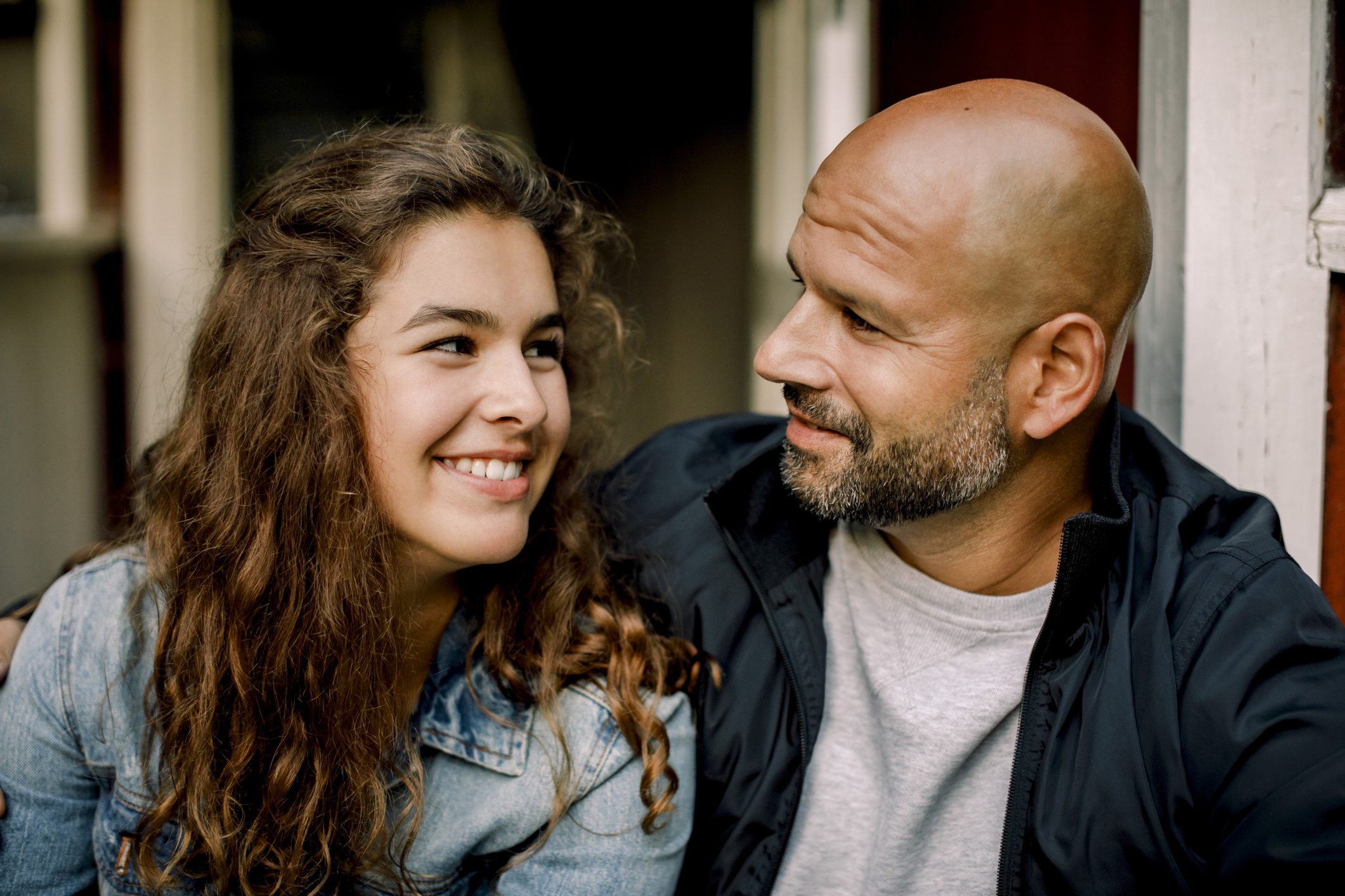 Teen daughter sits next to her father as they smile at one another
