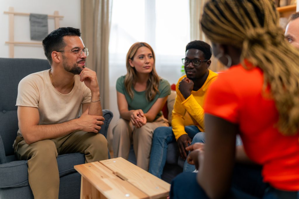 A group of adults sit in a circle in a comfortable domestic environment